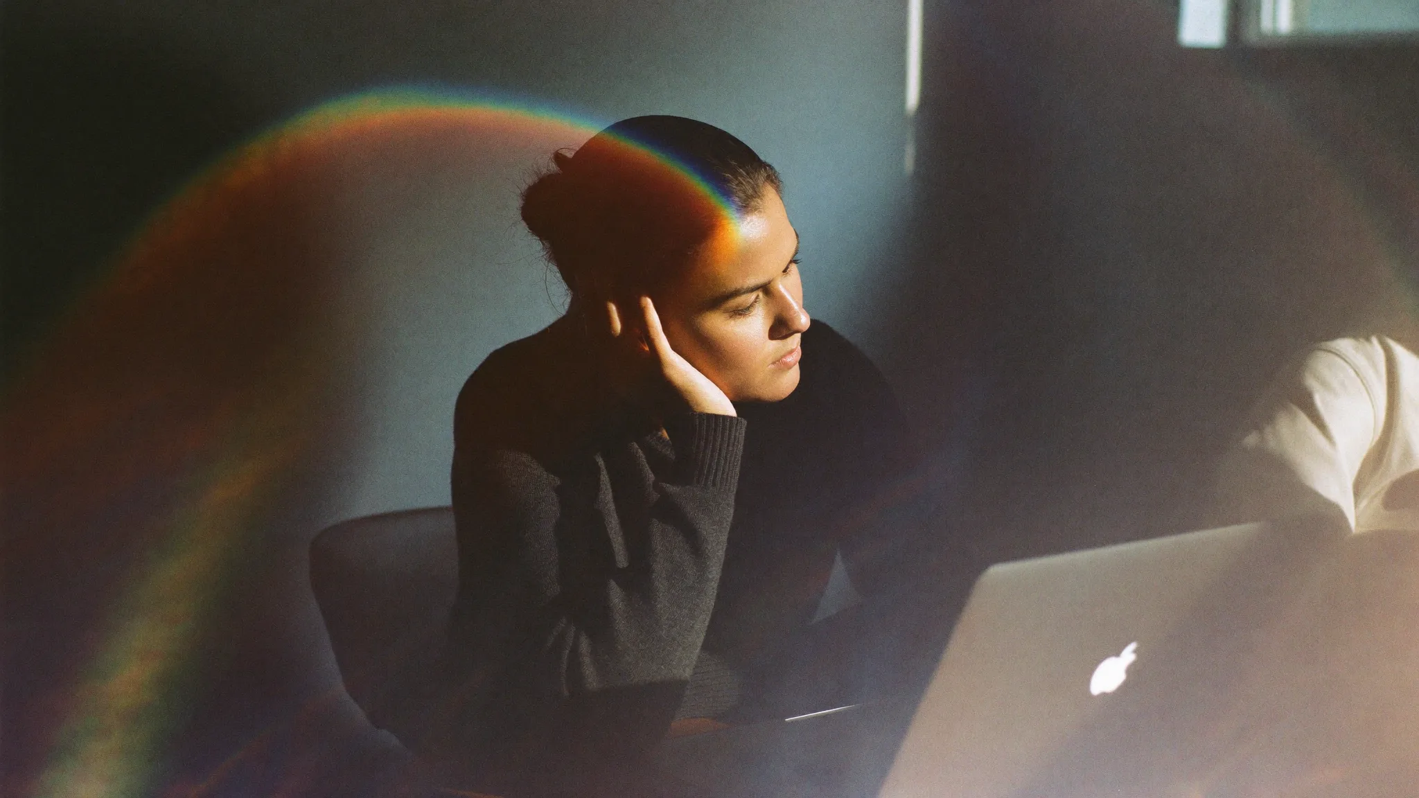 A woman listening on a call at her desk, a prism of light arcing across the wall beside her